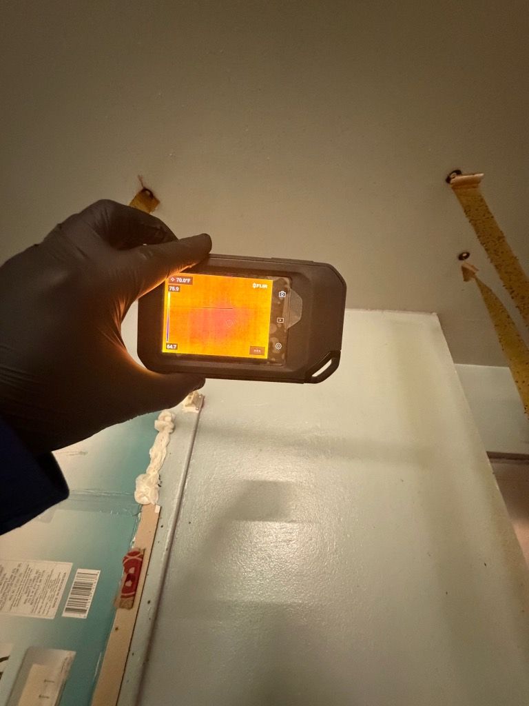 Technician pointing a thermal camera at a ceiling to look for hidden moisture